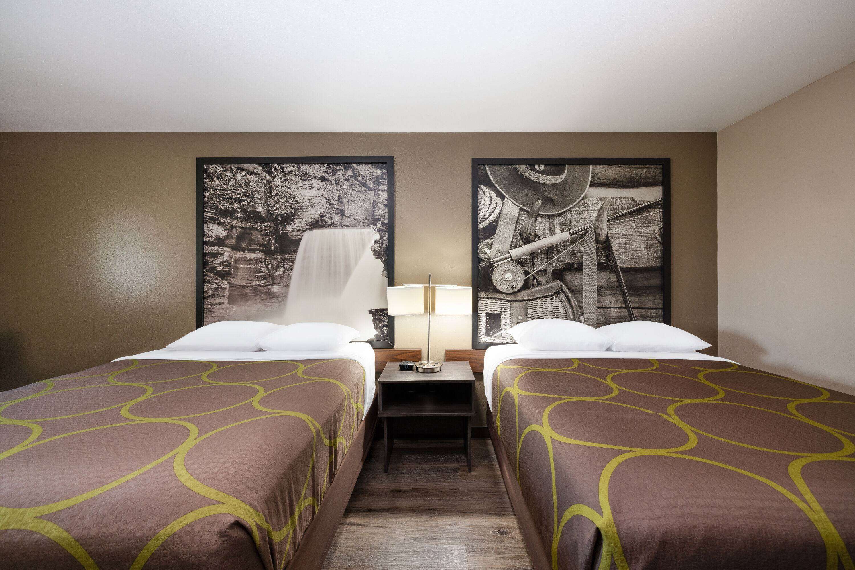 Una camera d'albergo con due letti singoli, un comodino con una lampada e due fotografie in bianco e nero appese alle pareti.