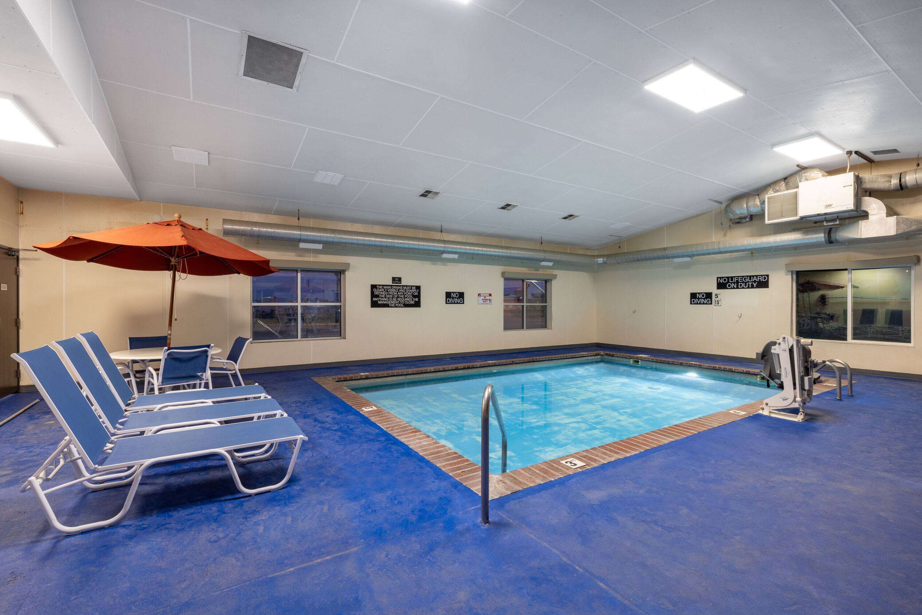 Une piscine intérieure avec des chaises longues bleues, un parasol rouge et un poste de surveillance pour le sauveteur.