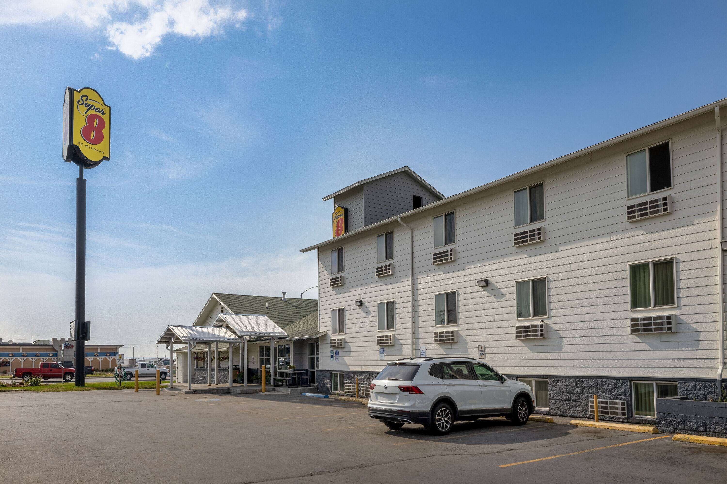 A motel with a white exterior, a covered entrance, and a parking lot with a white car.