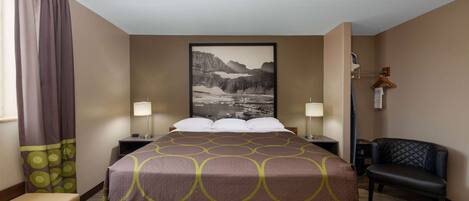 Habitación de hotel con cama, dos mesitas de noche, una silla, escritorio, lámpara, un cuadro en la pared y ventana con cortinas.