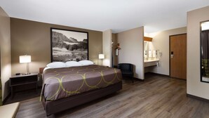 A hotel room with a large bed, bedside tables, a desk, a chair, a bathroom with a mirror, and a door.