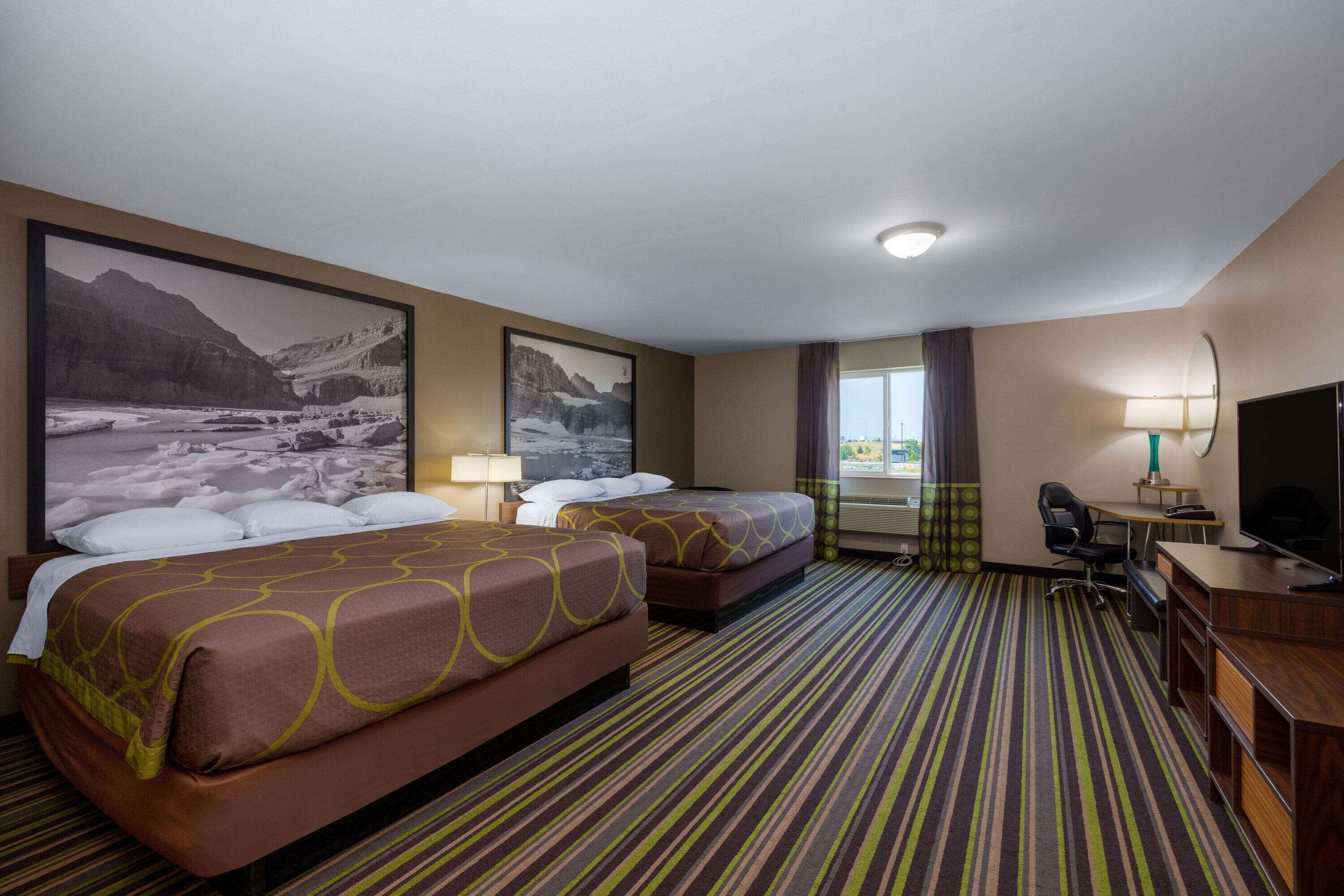Ein Hotelzimmer mit zwei Betten, einem Schreibtisch, einem Stuhl, einem Fernseher und einem großen Fenster.