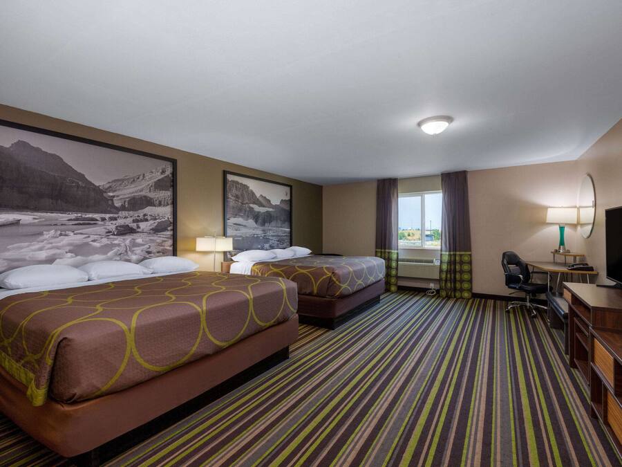 Ein Hotelzimmer mit zwei Betten, einem Schreibtisch, einem Stuhl, einem Fernseher und einem großen Fenster.