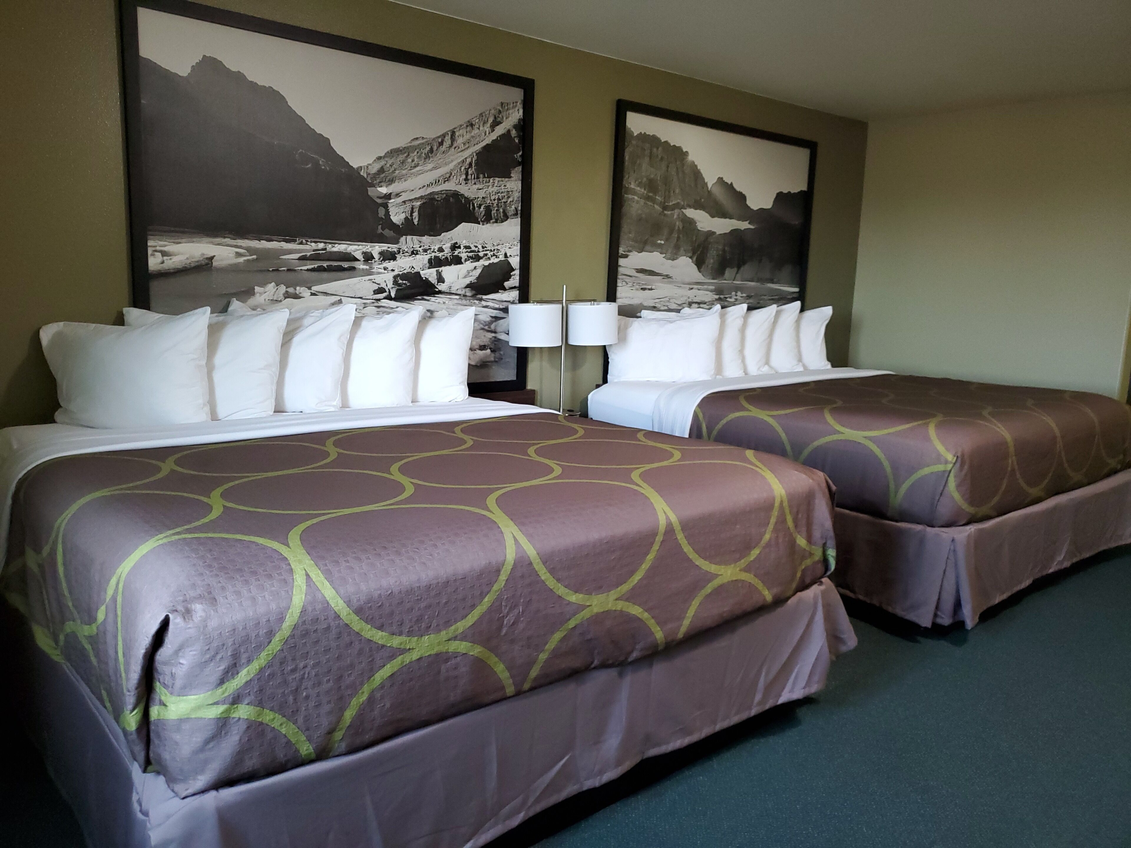 Habitación de hotel con dos camas, cada una con una colcha estampada, almohadas blancas y un cuadro grande con un paisaje montañoso en la pared detrás de las camas.