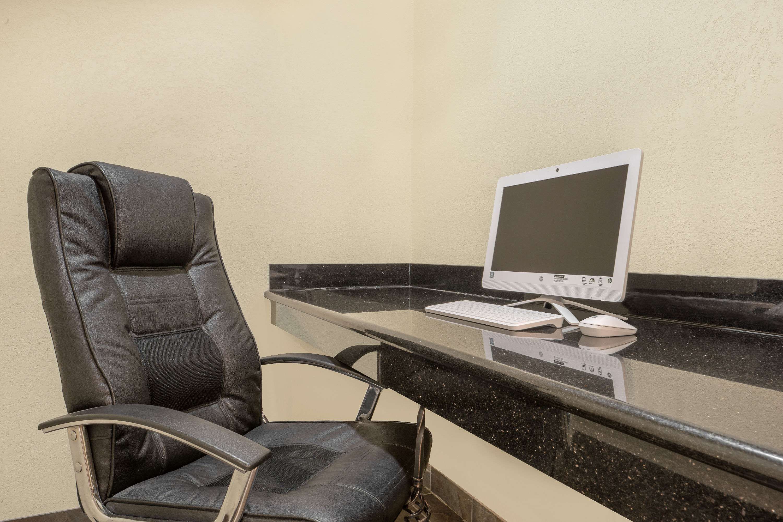 Una silla de oficina moderna con respaldo alto y apoyabrazos, ubicada junto a un escritorio de vidrio con una computadora de escritorio y un teclado.