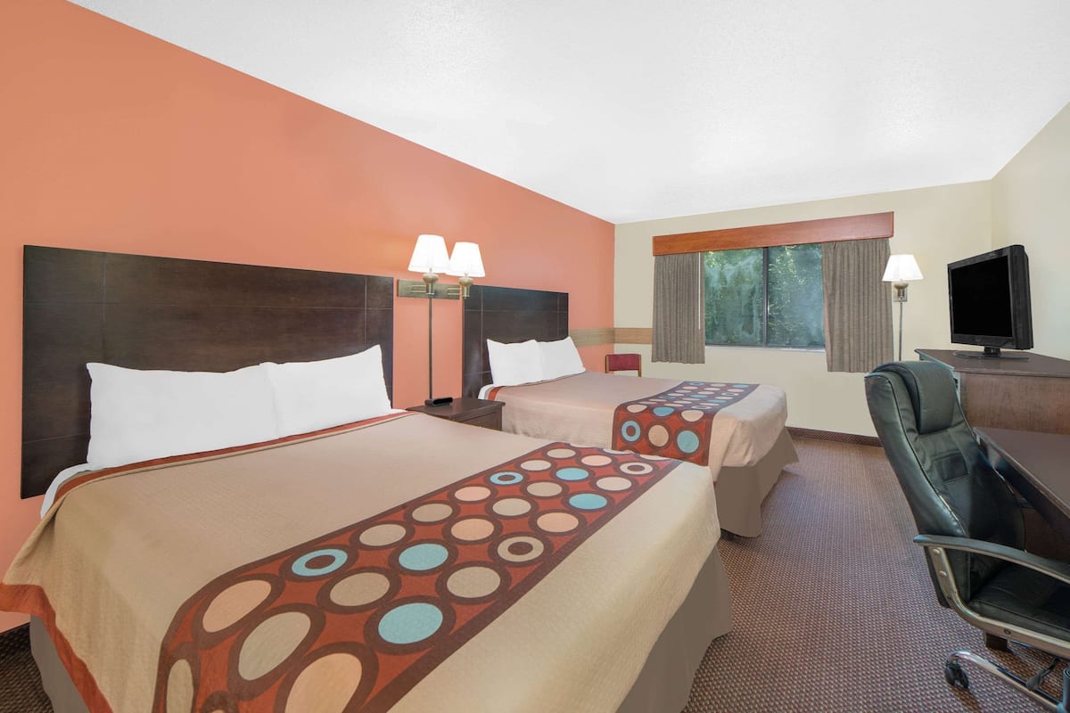 Una habitación de hotel con dos camas, un escritorio, una silla y un televisor.