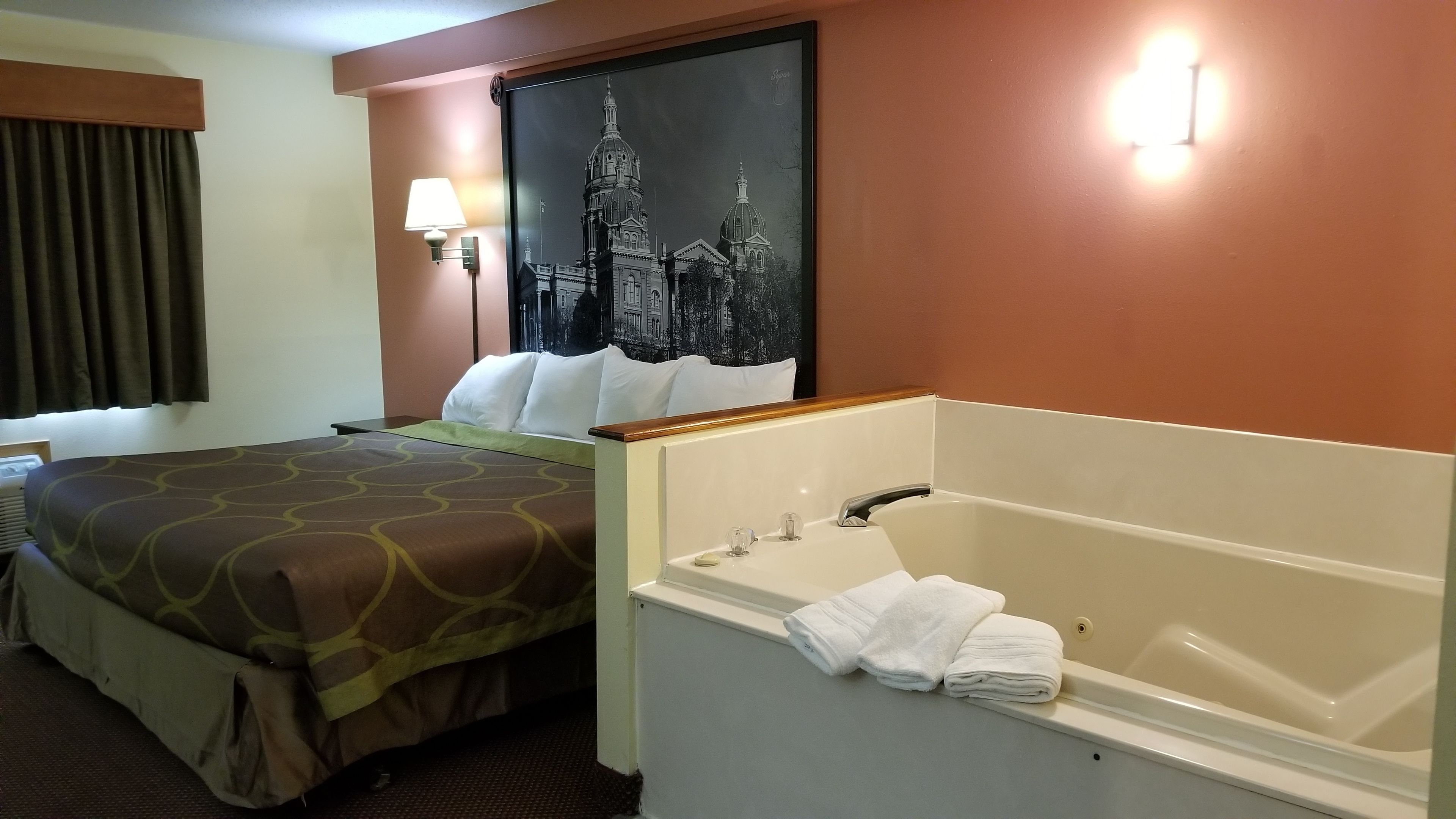 Habitación de hotel con cama, un cuadro grande de un paisaje urbano, un baño con bañera y una ventana con cortinas.