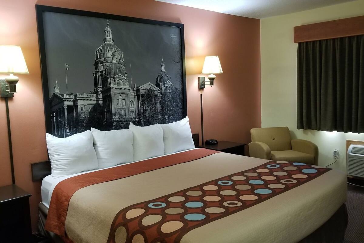Una habitación de hotel con una cama grande, dos lámparas de noche, una silla, una ventana con cortinas y un aire acondicionado instalado en la pared.