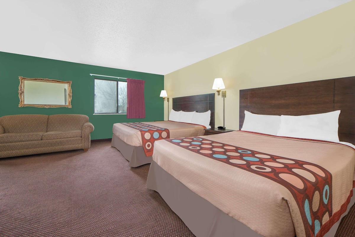 Habitación de hotel con dos camas, un sofá, una ventana con cortina y un espejo en la pared.