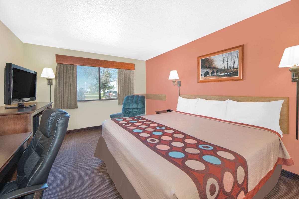 Habitación de hotel con cama, escritorio con televisor, silla y ventana con vista al exterior.