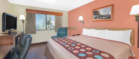 A hotel room with a bed, a desk with a television, a chair, and a window with a view of the outside.