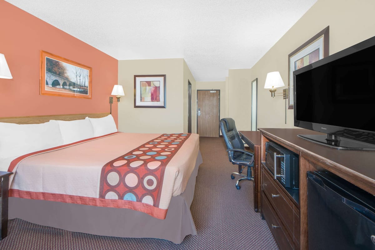 Habitación de hotel con una cama grande, un escritorio con televisor y una puerta que da a otra habitación.