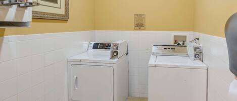 A laundry area with two washing machines, a tiled wall, and a framed picture.