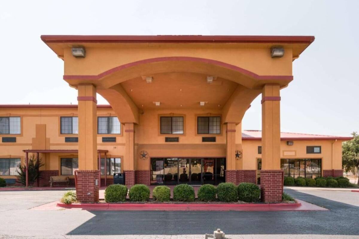 A hotel with a red roof, a covered entrance, and a parking lot.