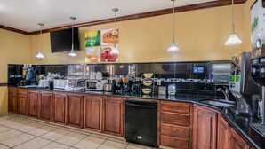 A modern kitchen with wooden cabinets, a black countertop, and stainless steel appliances. - Econo Lodge Lubbock I-27 (Lubbock)
