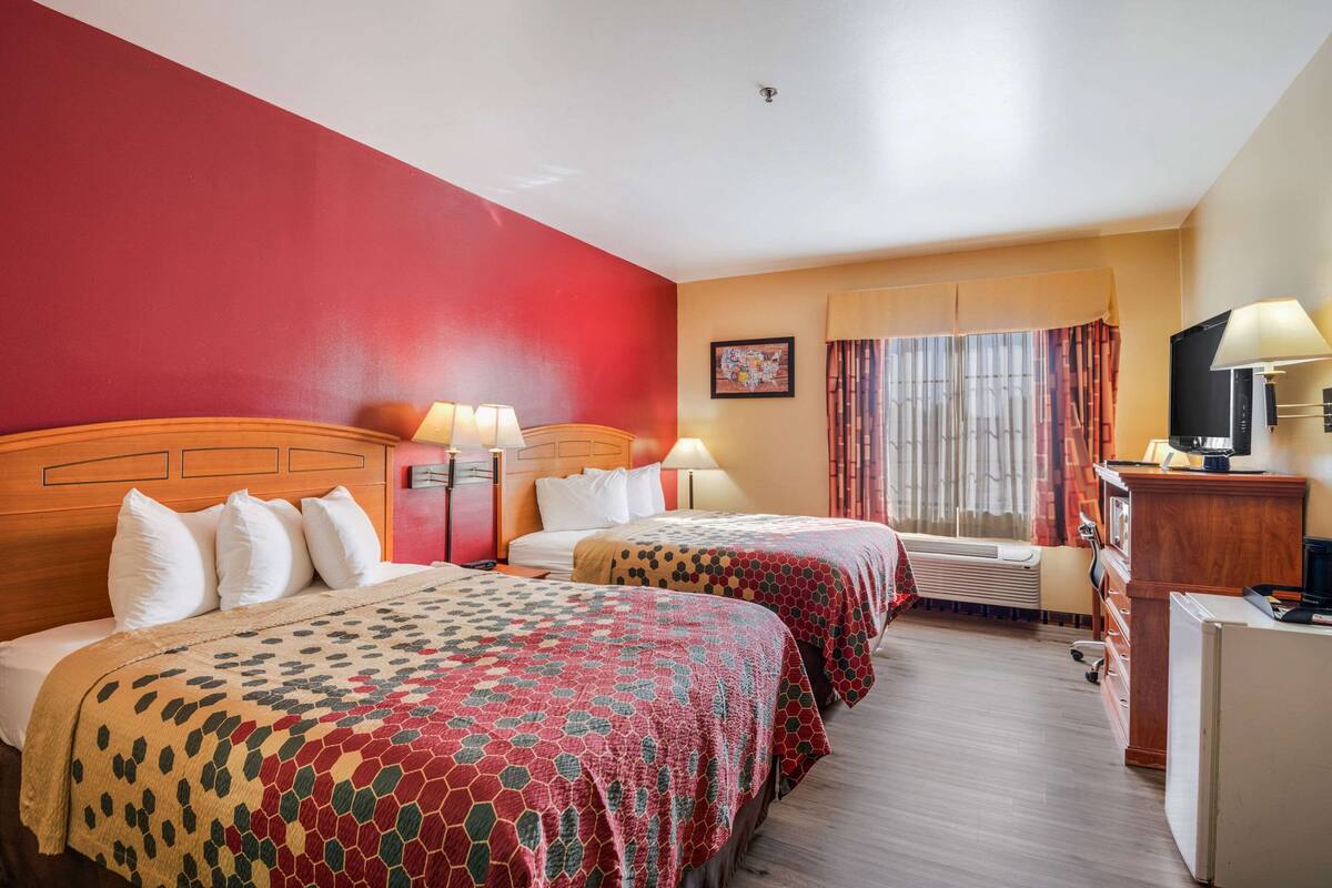 A hotel room with two beds, a television, a desk, and a window with curtains.