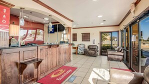 A reception area with a wooden counter, a red carpet with a logo, a seating area with leather chairs, and a large window offering a view outside. - Econo Lodge Lubbock I-27 (Lubbock)