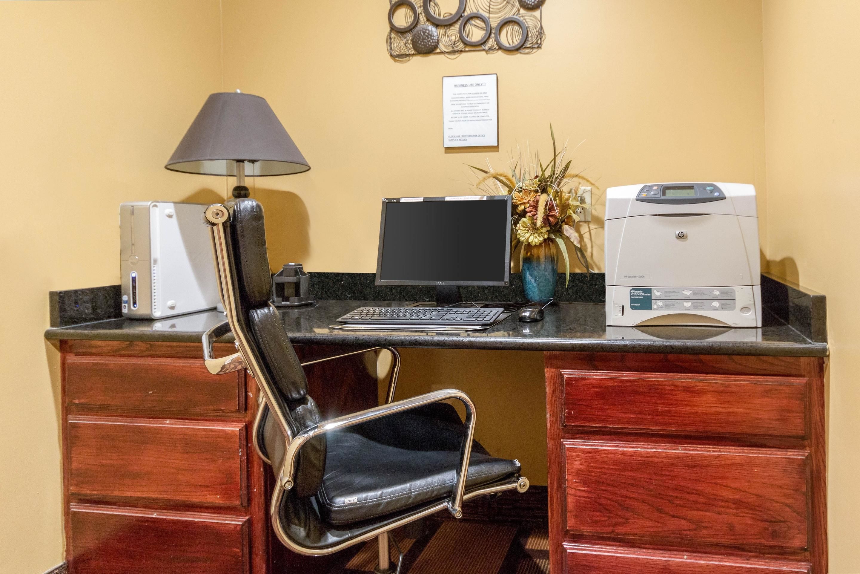 Een hotelkantoor met een bureau, computer, printer, lamp, stoel en een decoratief wandobject.