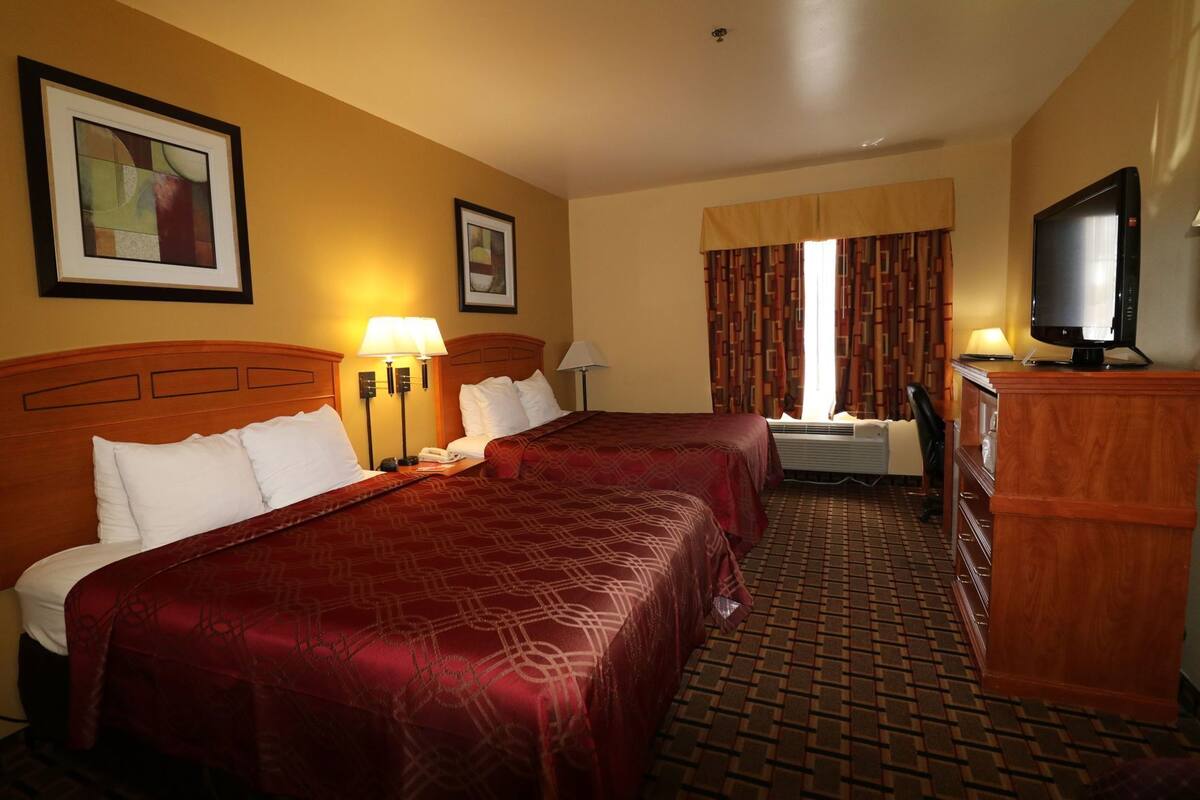 A hotel room with two beds, a television, a desk, and a window with curtains.