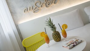 A room with a bed, a table with two drinks, a pineapple, and a yellow chair. - ibis Styles Nice Cap 3000 Airport (Saint-Laurent-du-Var)