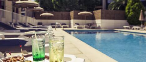 A poolside setting with a tray of drinks and olives, lounge chairs, and umbrellas in the background.