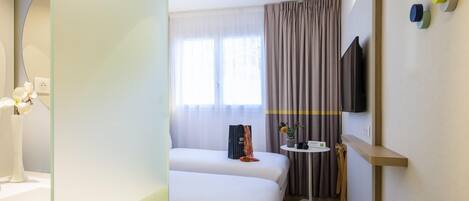 Una habitación de hotel con cama, mesita de noche, espejo, televisor y ventana con cortinas.