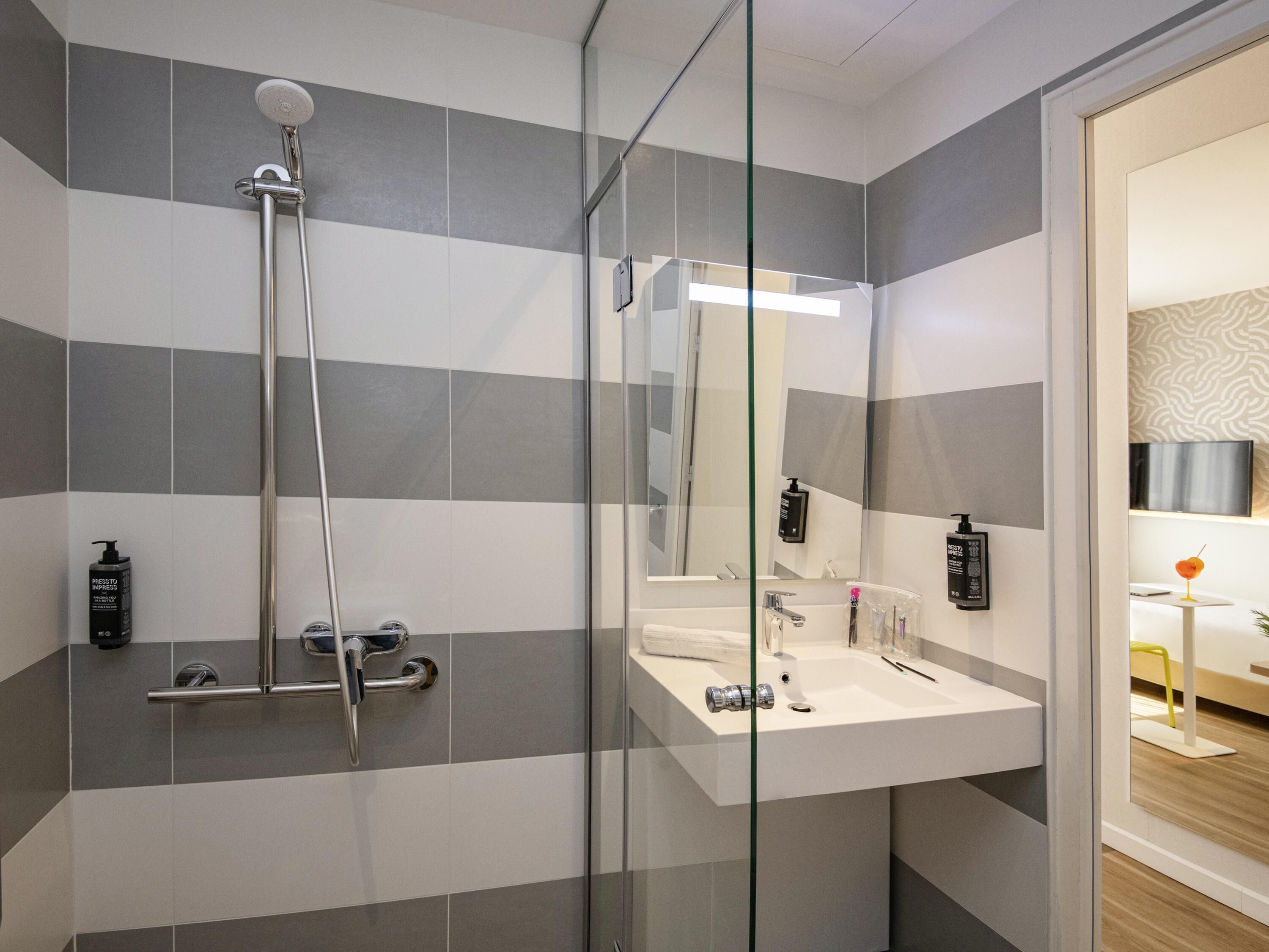 Une salle de bain moderne avec une douche à l’italienne en verre, un lavabo blanc et un grand miroir.