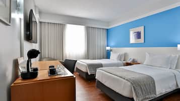 Una habitación de hotel con dos camas, un escritorio con computadora, una silla y un televisor montado en la pared.