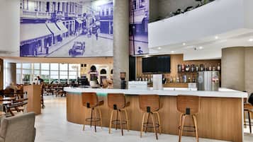 A modern bar area with wooden stools, a bar counter, and a large mural depicting a street scene.