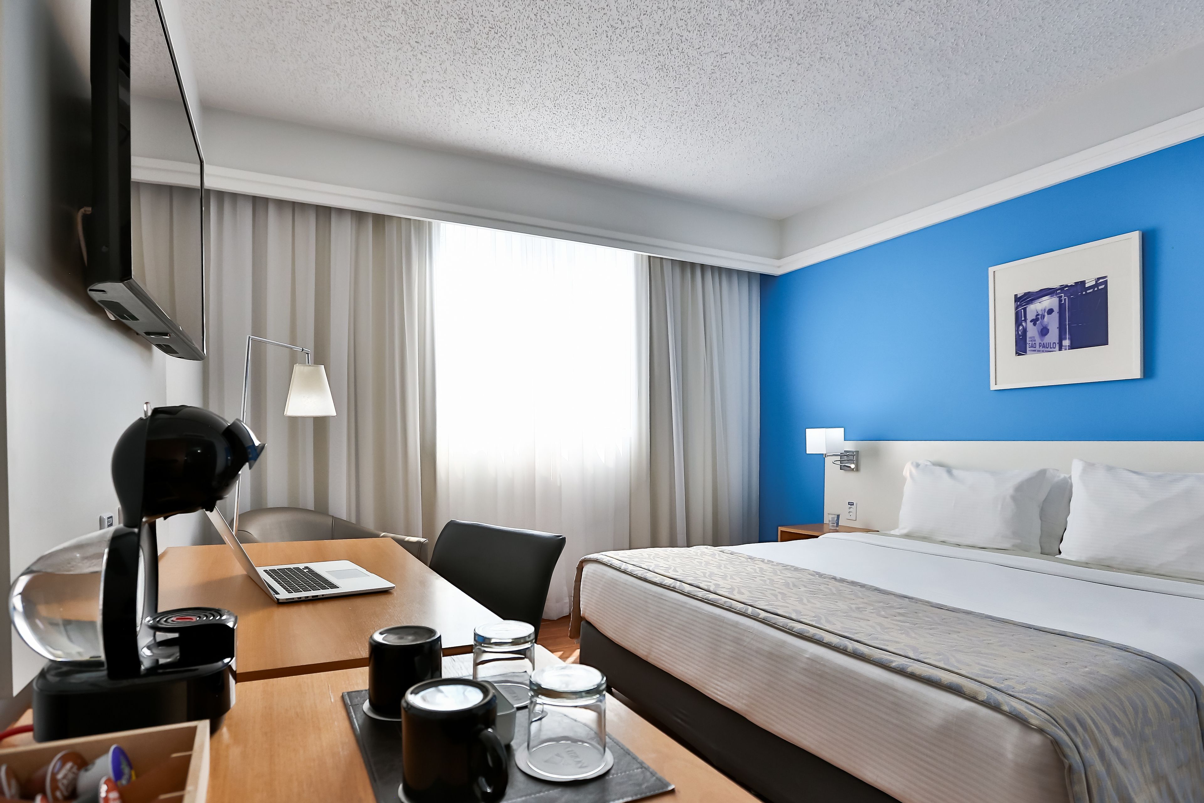 Una habitación de hotel con una cama, un escritorio con una computadora portátil, una cafetera y un televisor.