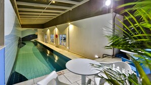 An indoor swimming pool with a tiled floor, a ceiling with skylights, and a seating area with a table and chairs. - SLAVIERO Downtown São Paulo (São Paulo)