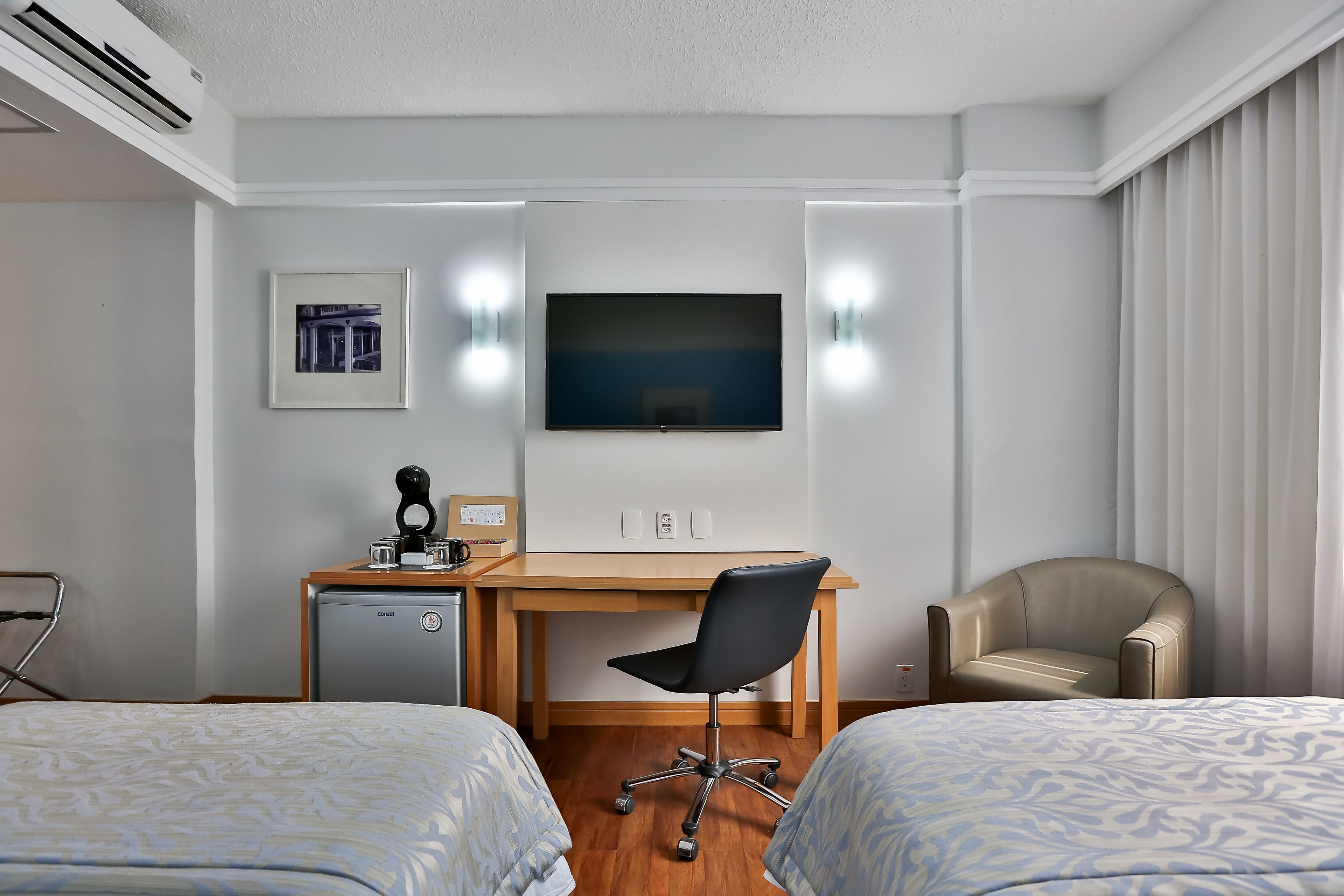 Habitación de hotel con dos camas, un escritorio, una silla, un televisor y un minibar.