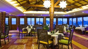 Un restaurant avec des poutres en bois, des tables dressées pour le repas et de grandes fenêtres offrant une vue sur la mer.
