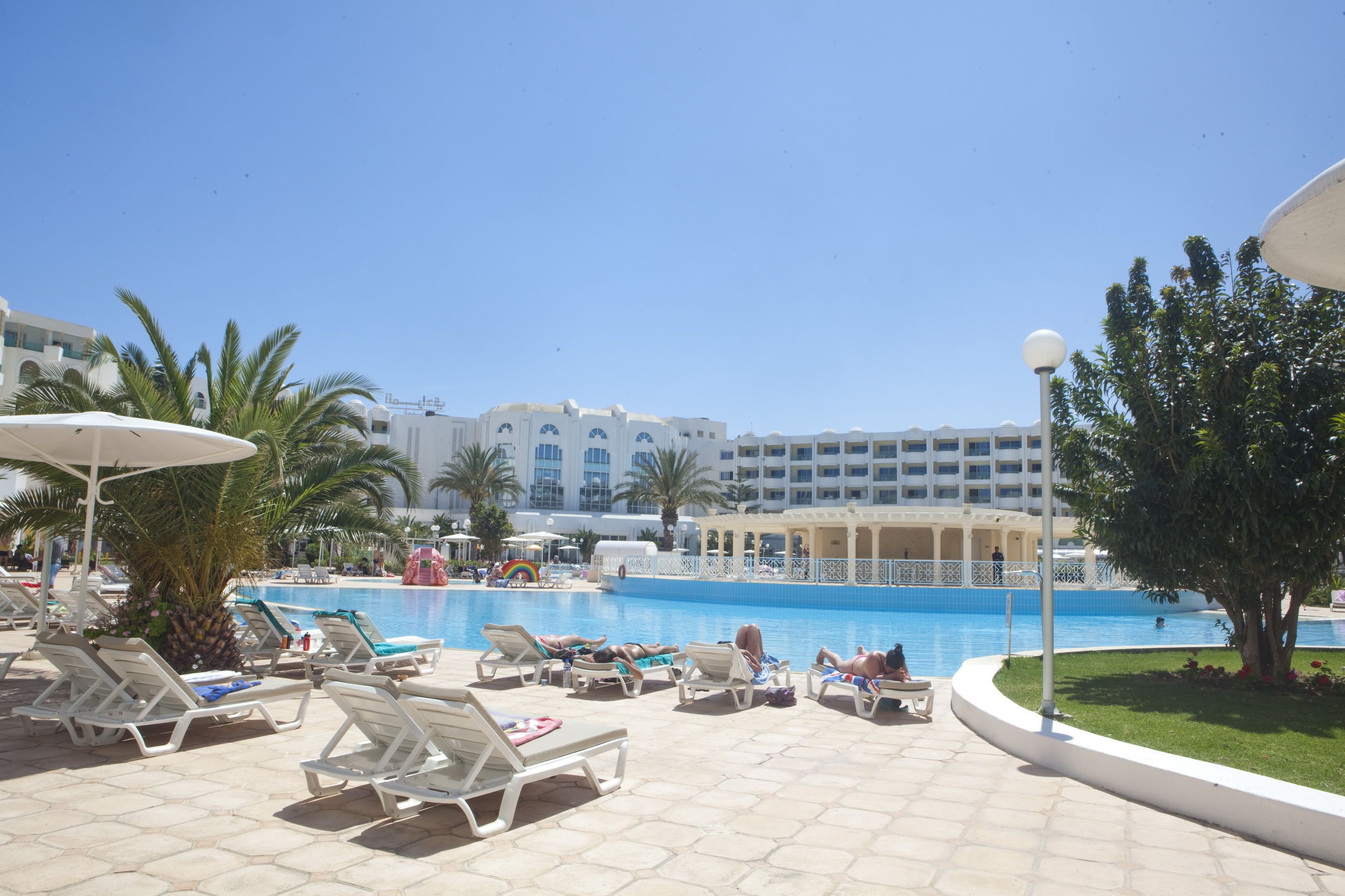 A poolside area with lounge chairs, umbrellas, and a large building in the background.