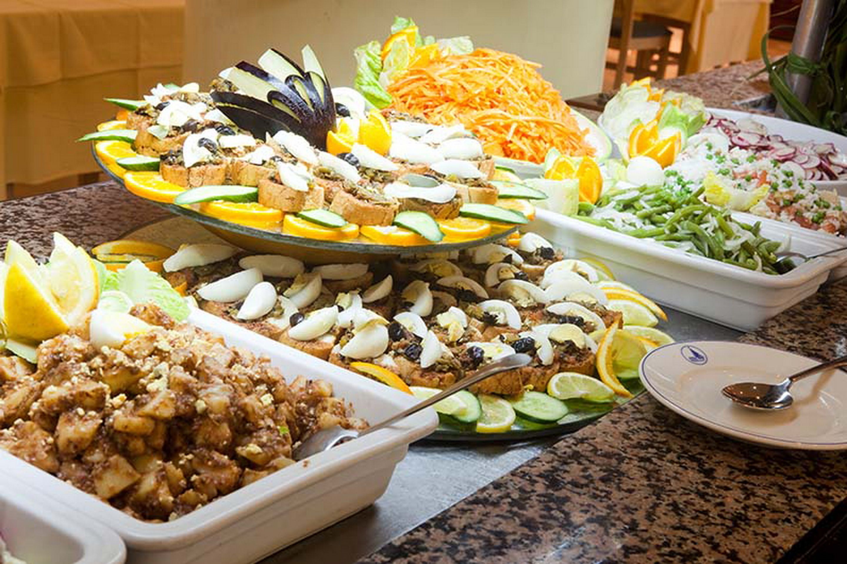 Un bufé con diversos platos, incluyendo ensaladas, frutas y un postre en capas.