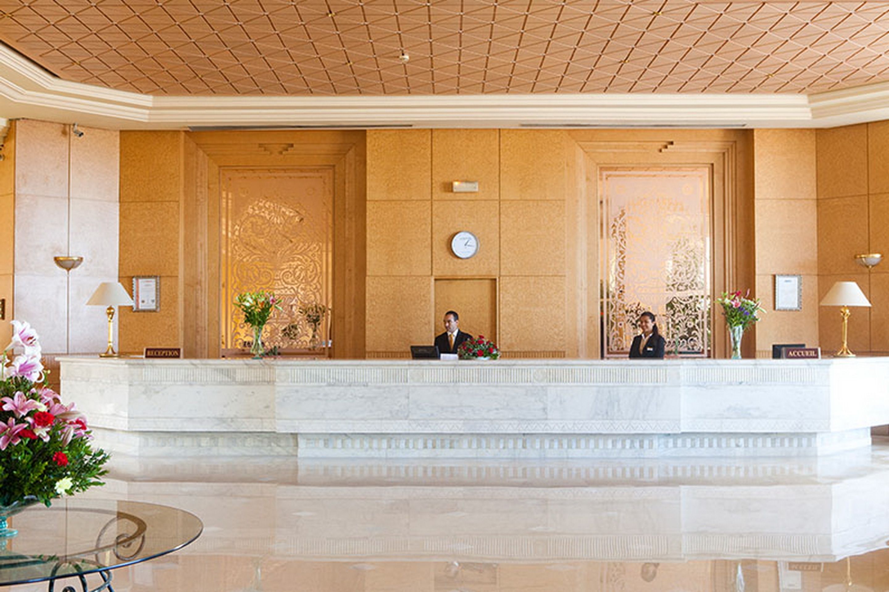 A reception area with a marble counter, two receptionists, and a clock on the wall.
