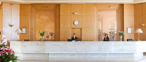 A reception area with a marble counter, two receptionists, and a clock on the wall.