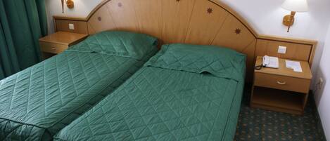 A double bed with green bedding, two bedside tables with lamps, and a patterned carpet.