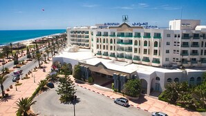 Un hôtel doté de nombreux balcons, offrant une vue sur la plage et disposant d’un parking avec des voitures.