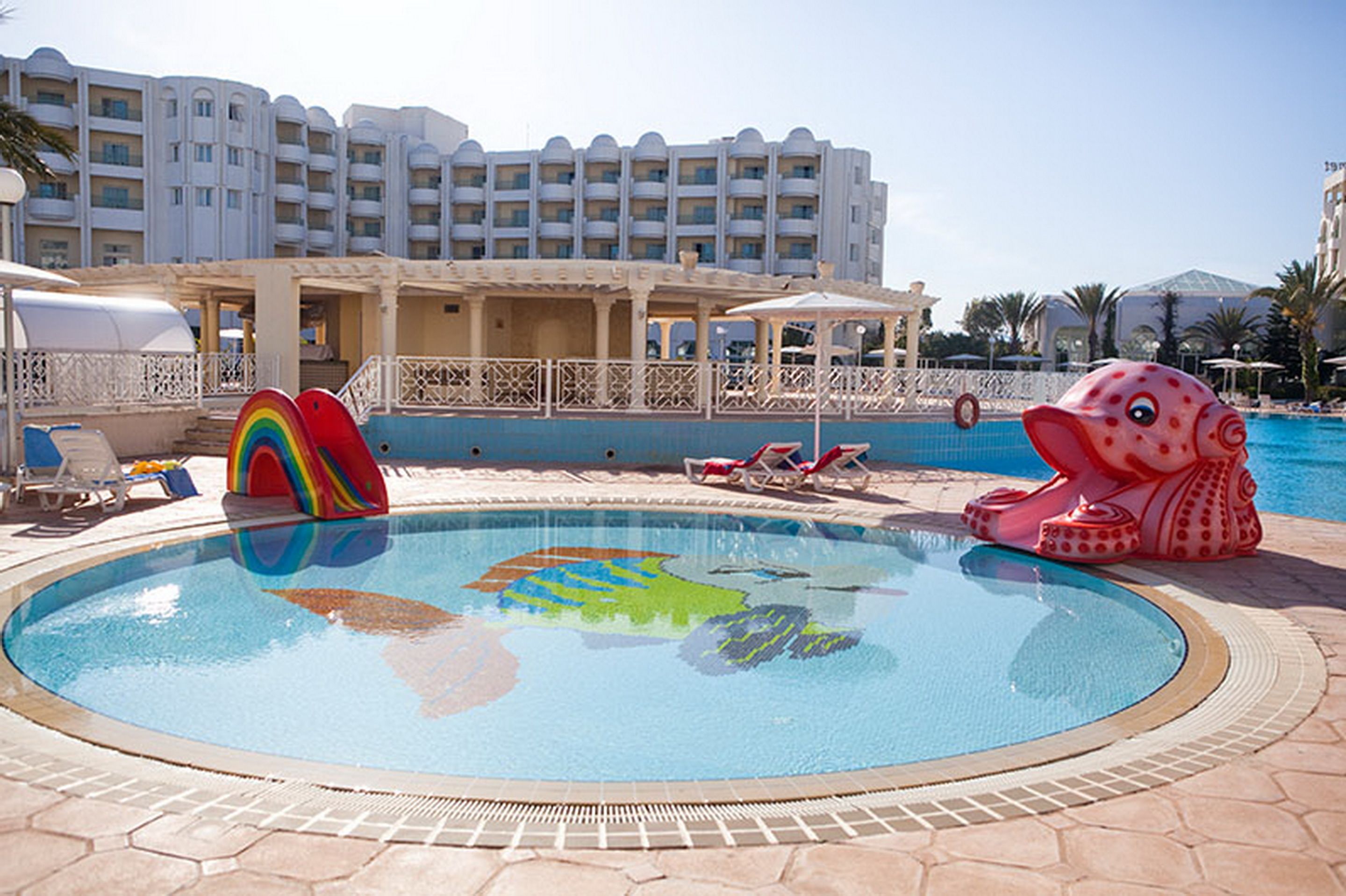 Une piscine avec un toboggan coloré et une grande décoration gonflable en forme de poulpe.