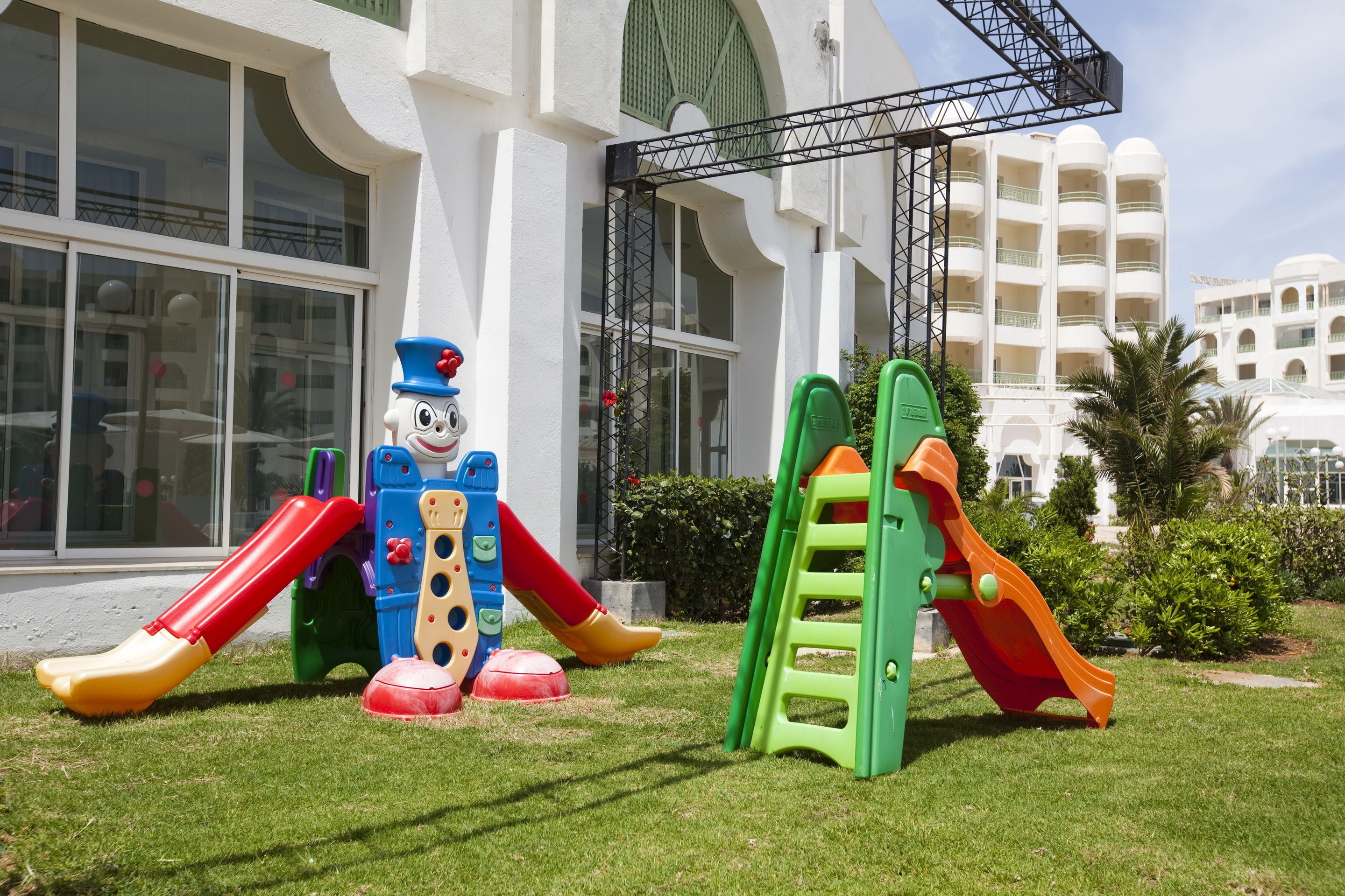 Un parque infantil con toboganes y una estructura para escalar frente a un edificio con ventanas amplias y balcones.