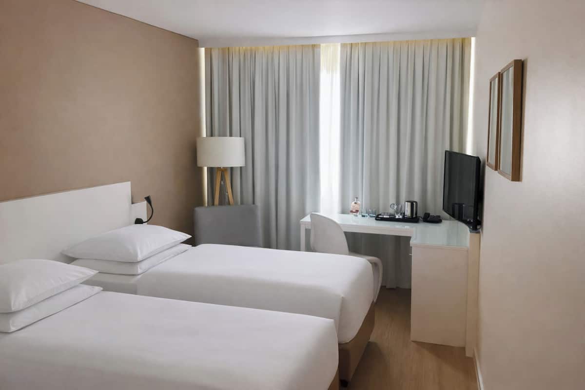 Une chambre d’hôtel avec deux lits, un bureau, une chaise, une télévision et une fenêtre avec des rideaux.