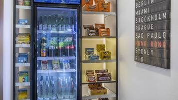 Ein Getränkeautomat mit verschiedenen Getränken und Snacks, umgeben von Regalen voller verpackter Lebensmittel.