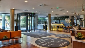 A modern hotel lobby with a reception desk, seating area, and a rotating door. - Hotel Frankfurt Messe affiliated by Meliá (Frankfurt)