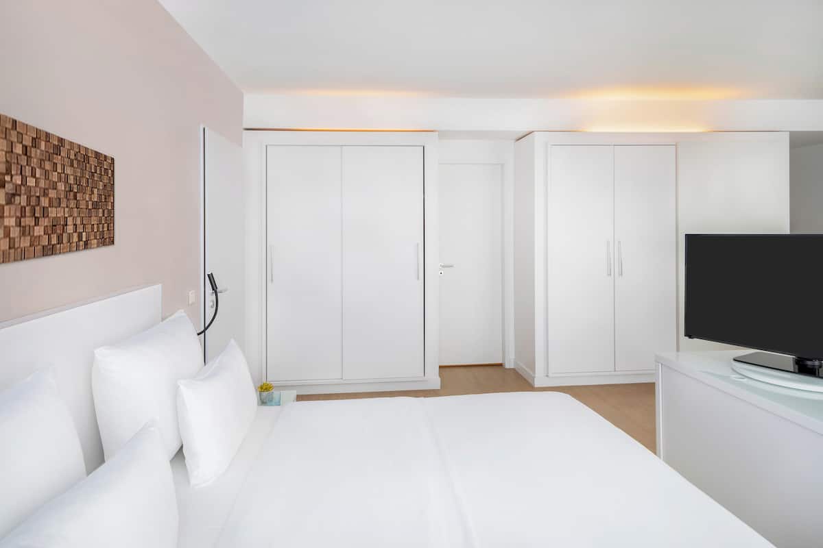 Une chambre d’hôtel avec un lit, une télévision, des armoires blanches et une œuvre d’art murale.