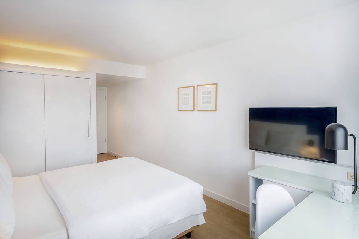 Une chambre d’hôtel moderne équipée d’un lit, d’un bureau, d’une télévision et de deux tableaux encadrés accrochés au mur.