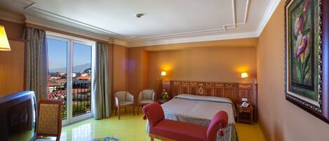 A hotel room with a bed, a television, a sofa, a desk with a lamp, and a painting on the wall.