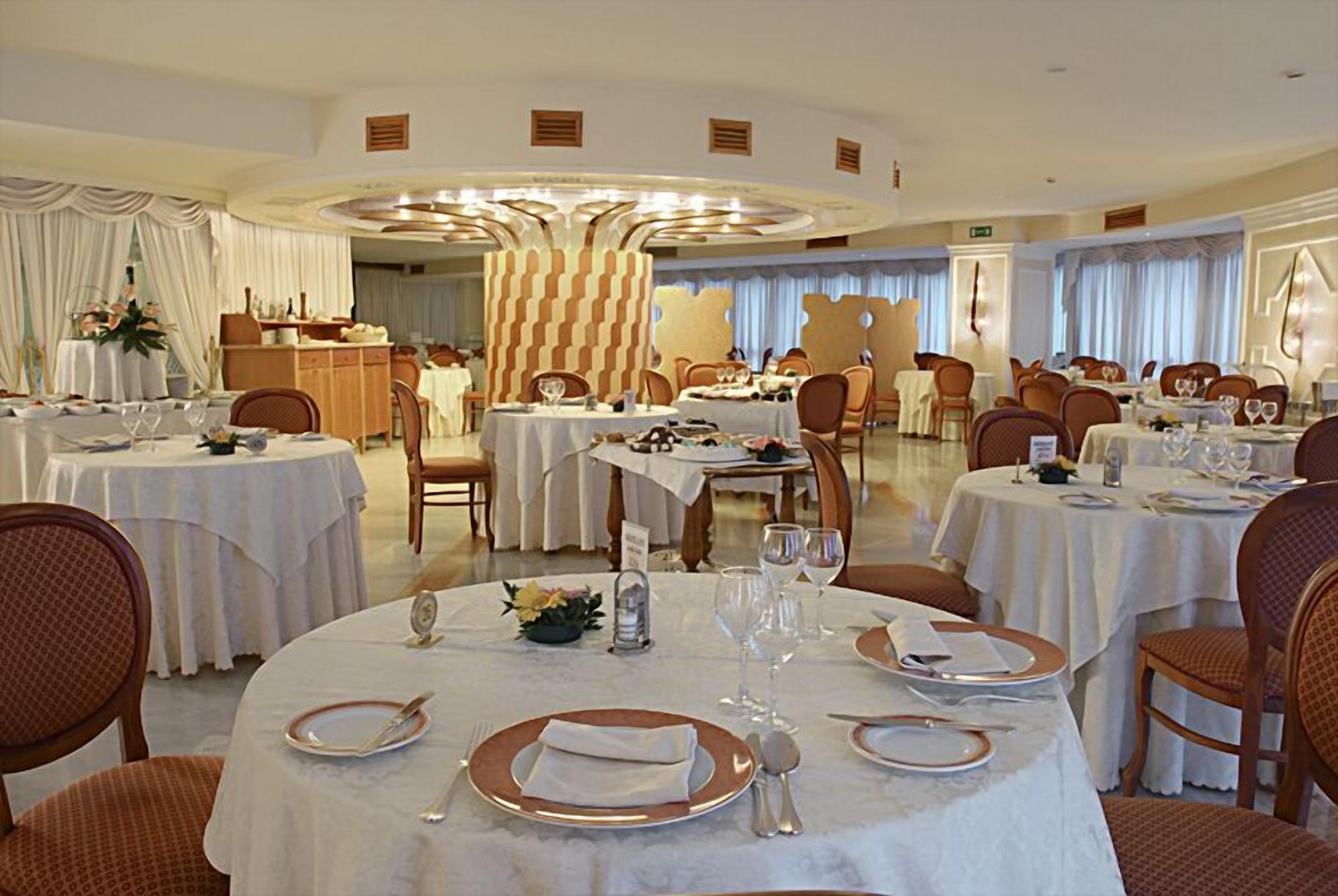 A dining area with round tables set for service, featuring white tablecloths and gold-rimmed plates.