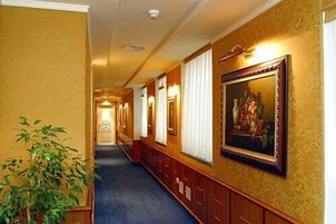 A hotel hallway with a blue carpet, wooden paneling, and a framed painting on the wall.