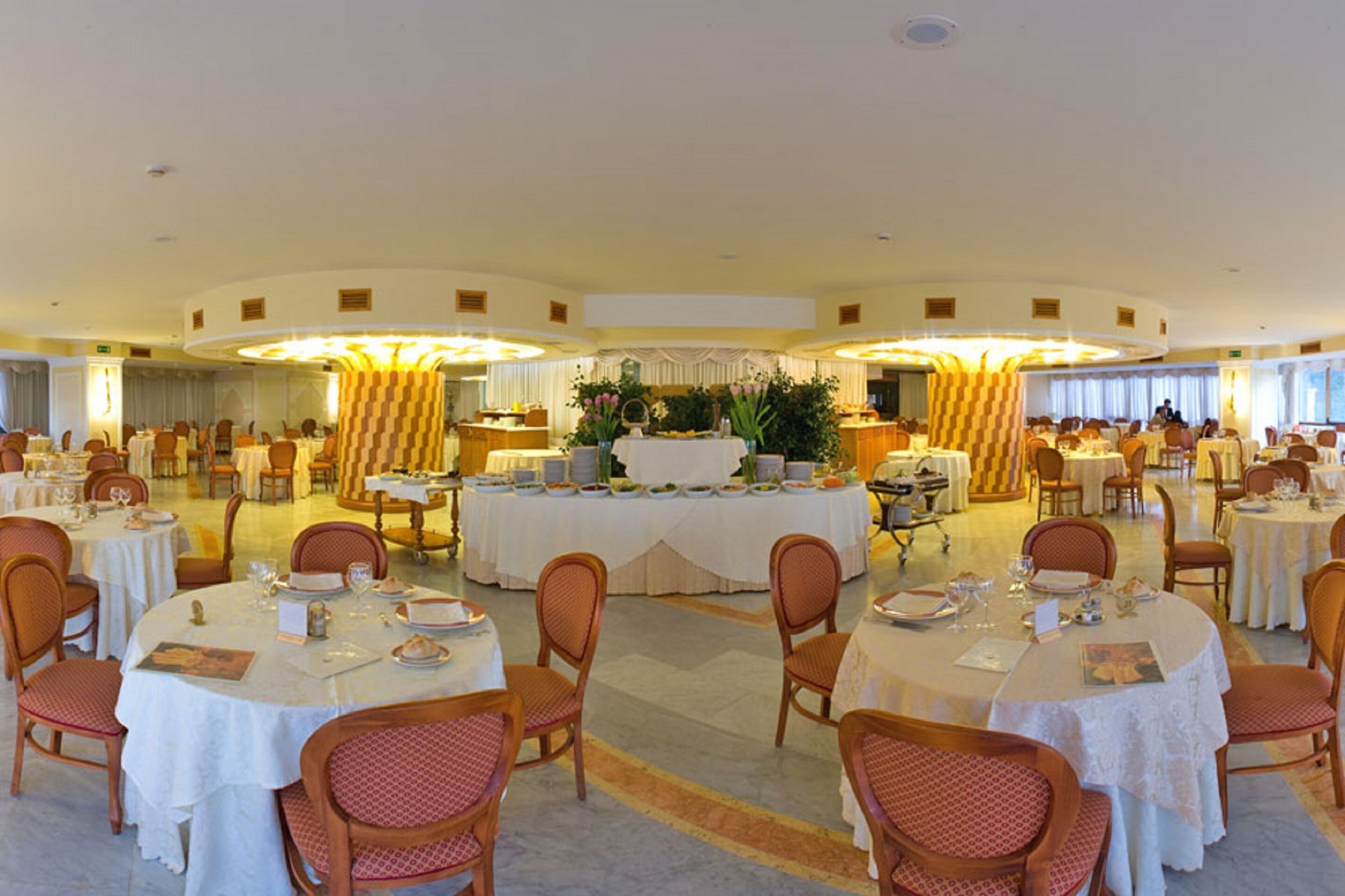 A large banquet hall with round tables, chairs, and a central floral arrangement.